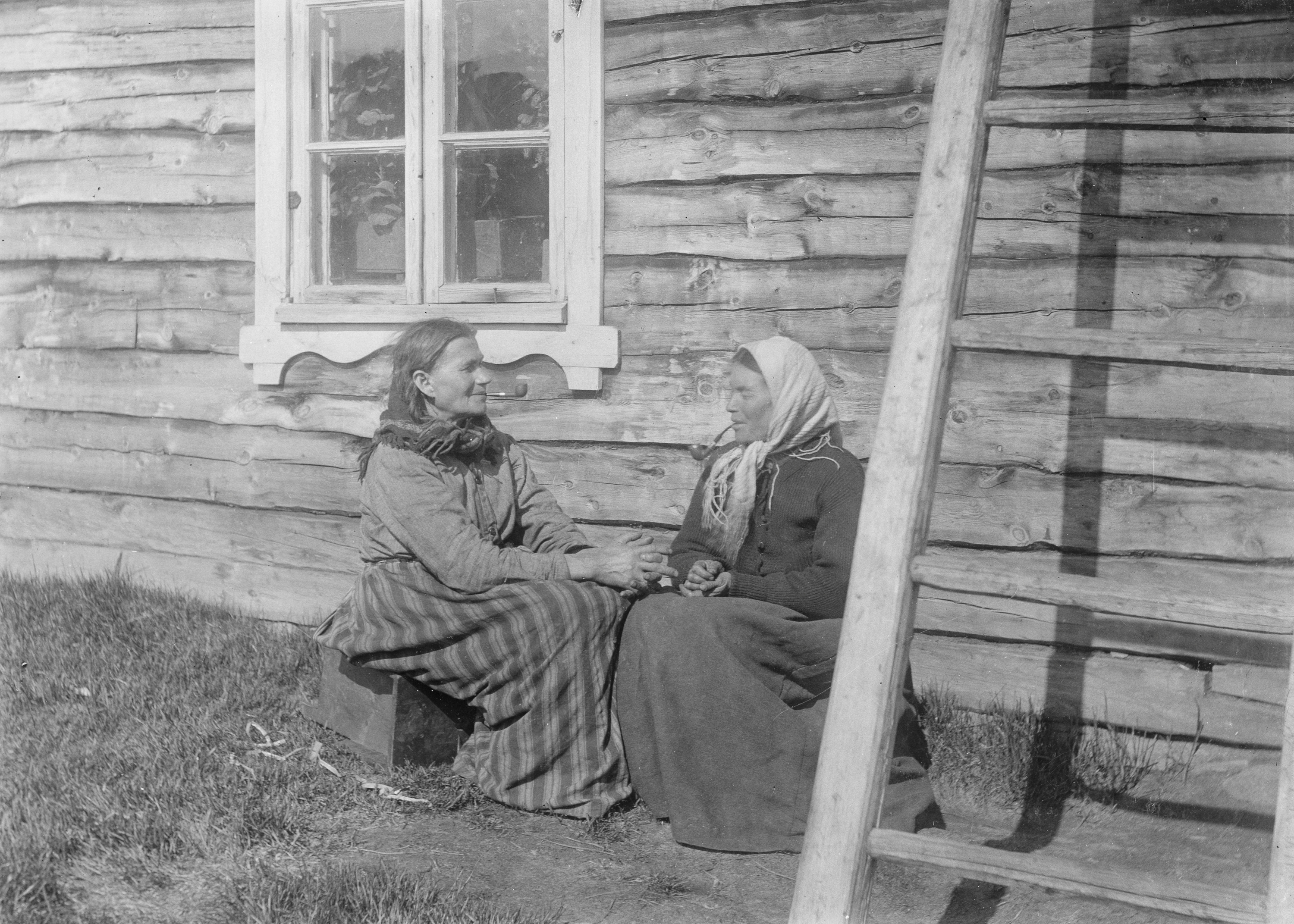 Svart-hvitt foto av to kvenske damer som sitter utenfor et hus.