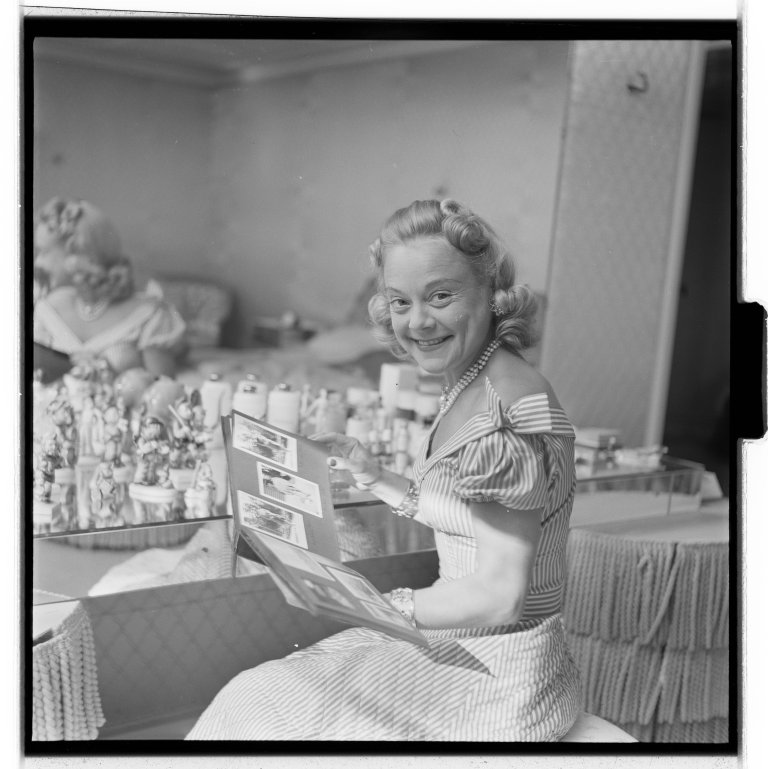 Svart-hvitt foto av kvinne som sitter ved et sminkebord. 