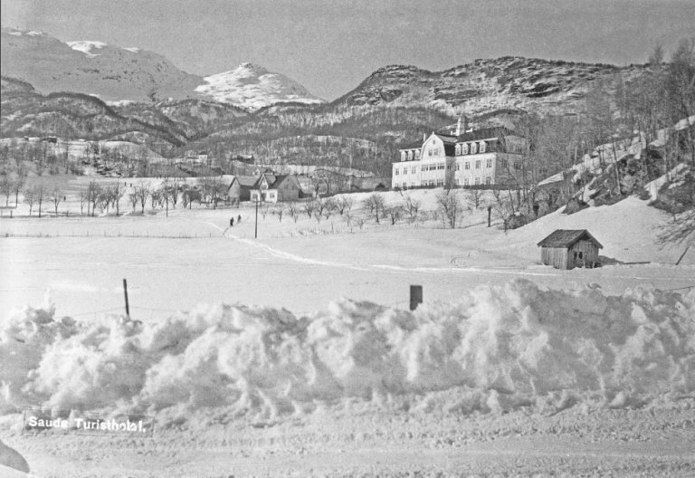 Vinterfoto av hotellet med snøkledde fjell i bakgrunnen.