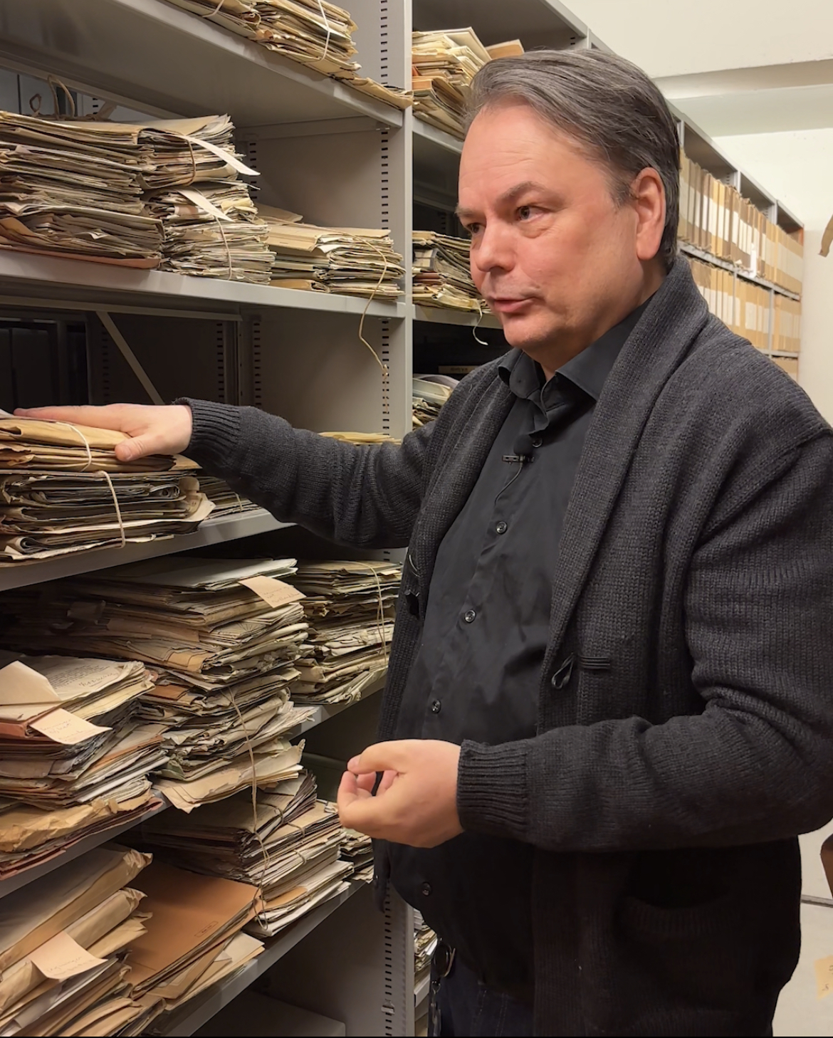 Foto av mann som står i et arkivmagasin med gamle arkiver