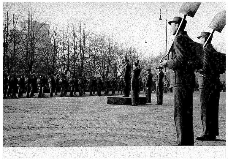 Mannskapa i Norges Arbeidstjeneste var uniformerte og dreiv eksersis, men med spade istadenfor gevær. Her frå ei mønstring på Karl Johan i oktober 1941. Mannen på plattformen er general Carl Frølich Hanssen, øvste sjef for AT. RA/PA-1209 NTBs krigsarkiv/Ue/0096.