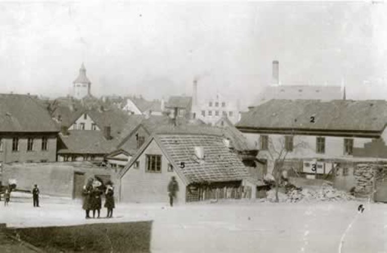 Biletet viser bygningskomplekset på St. Petersgjerde etter at rivinga hadde teke til i 1897. Valberg-tårnet ruvar i bakgrunnen. Bygningane er: Arbeidsanstalten (1), sjukehuset (2), sinnsjukeasylet (Dollhuset) (3) , Spindhuset/hospitalet (4) og vaktmeisterbustaden (5). Restar av det gamle steingjerdet viser til høgre. Foto: Ukjend. A. Bærheim sitt arkiv. Statsarkivet i Stavanger.